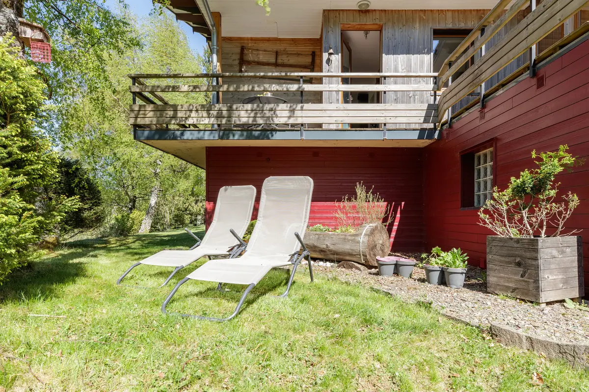 Chaises longues dans le jardin devant la façade rouge du chalet